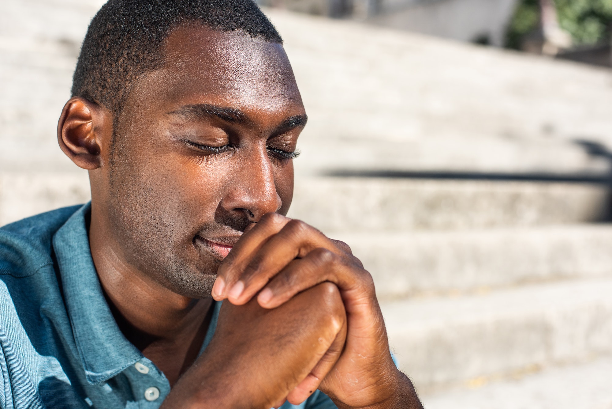 Close up young black man with eyes closed praying outside
